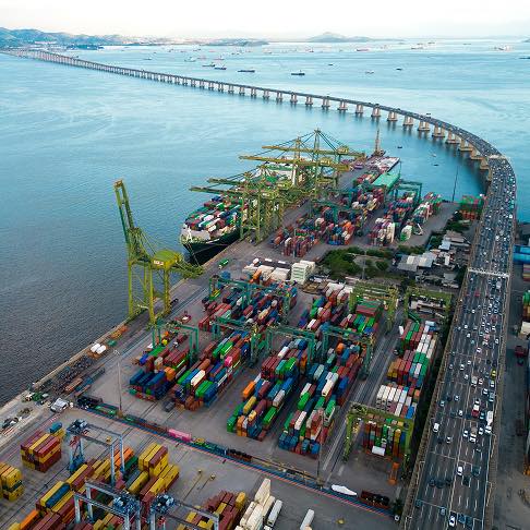 Port maritime animé avec grues, conteneurs et un long pont au-dessus de l'eau.