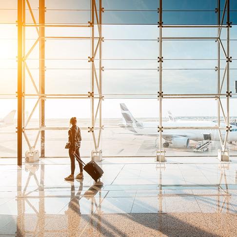 Femme avec une valise à l'aéroport, regardant un avion par la fenêtre